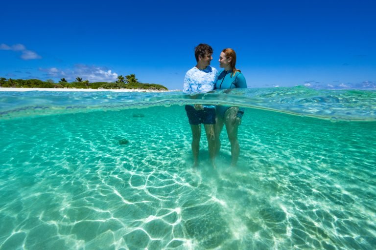 Two Co-Exist Projects researchers standing in clear shallow water, shot half above and half below the surface