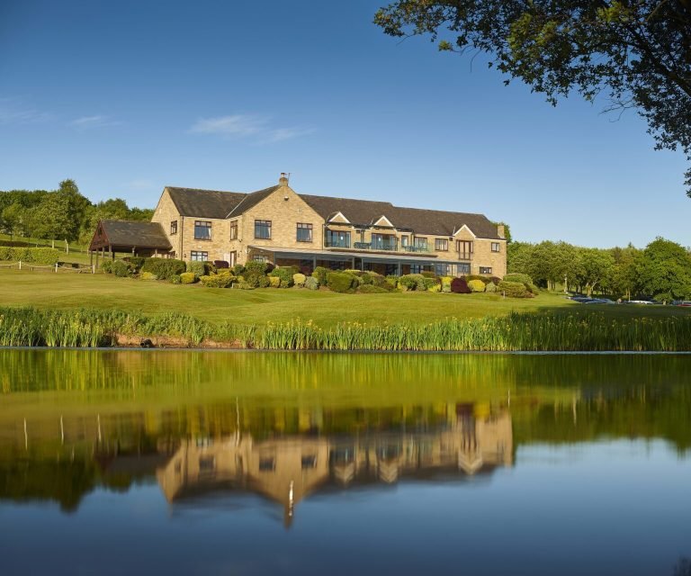 The Houghwood clubhouse reflected in the lake, with the golf course rising behind it