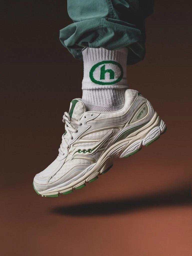 A preloved white Saucony ProGrid trainer photographed against a warm brown backdrop for the Footprint Shoes homepage