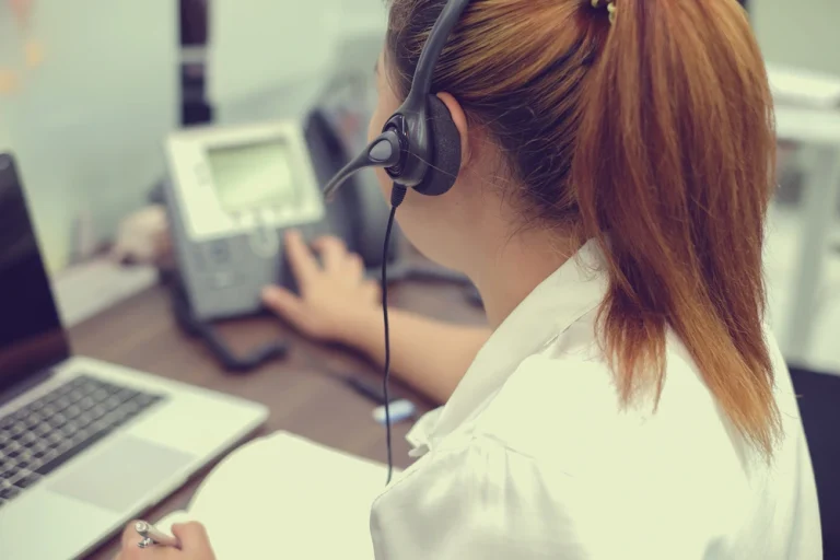 A call handler wearing a headset at a desk with a phone and laptop